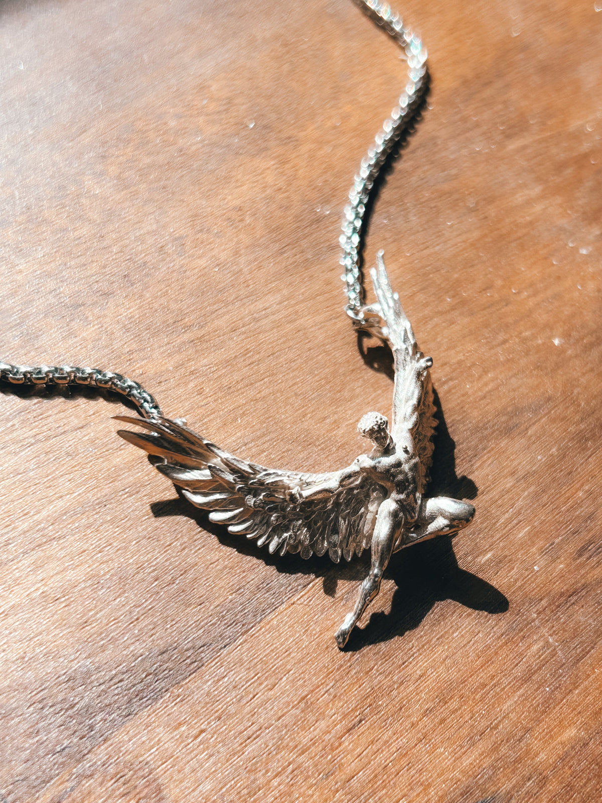 Silver Icarus pendant necklace on a wooden surface