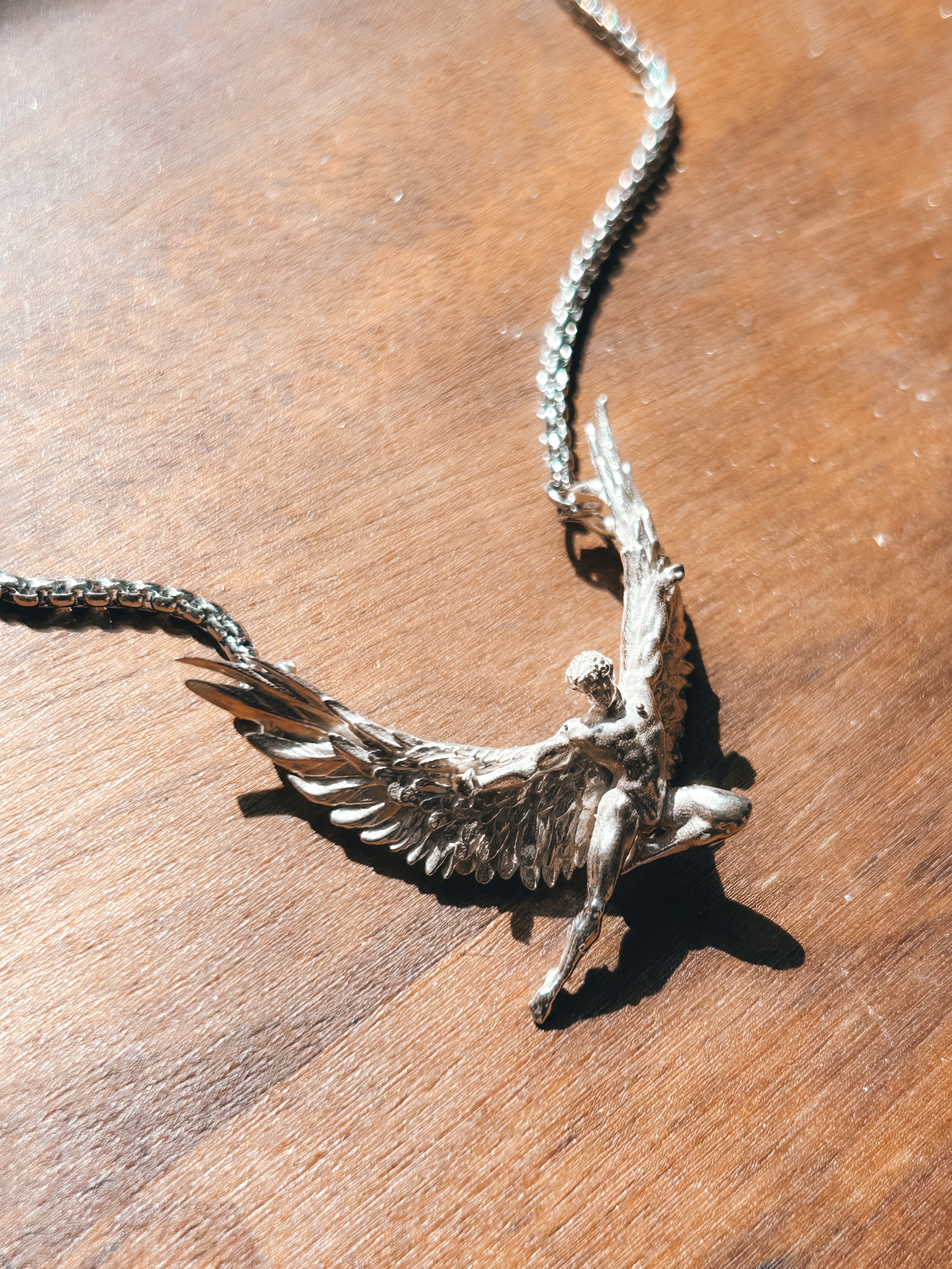 Silver Icarus pendant necklace on a wooden surface